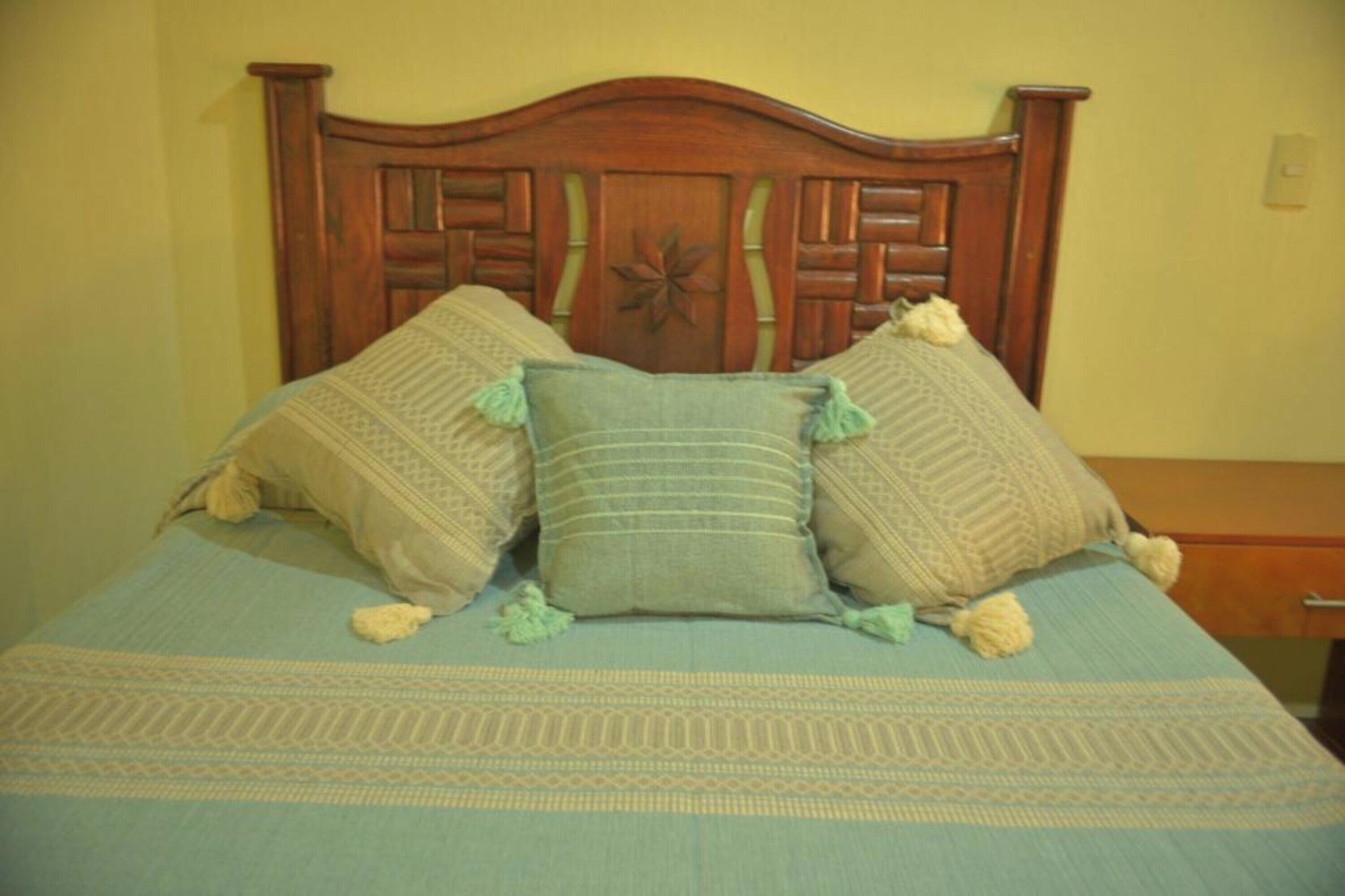 A bed with a wooden headboard, a patterned bedspread, and two decorative pillows.