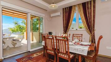 A dining area with a table set for four, wooden chairs, a patterned rug, and a view through a glass door.