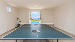 A ping pong table with a paddle and ball, a window with bars, and a view of a swimming pool and mountains. - Pool Villa Panorama Mojdez /w Sea View (Mojdez)