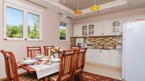 A dining area with a table set for four, wooden chairs, a white tablecloth, and a window with a view of greenery. - Pool Villa Panorama Mojdez /w Sea View (Mojdez)