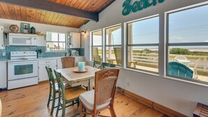 A kitchen with wooden cabinets, a white stove, and a dining area with wicker chairs and a table. - Gulf Coast Views! Coastal Winter Gem in Galveston (Galveston)