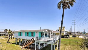 A two-story house with a balcony, a staircase leading to the upper floor, and a fenced yard with palm trees. - Gulf Coast Views! Coastal Winter Gem in Galveston (Galveston)