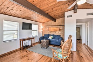A living room with a wooden ceiling, a blue sofa, a wooden coffee table, and a wicker chair. - Gulf Coast Views! Coastal Winter Gem in Galveston (Galveston)