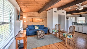 A cozy living area with a wooden ceiling, a blue sofa, a small table, wicker chairs, and a kitchen in the background. - Gulf Coast Views! Coastal Winter Gem in Galveston (Galveston)