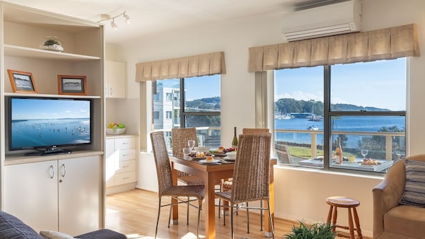 Una sala de estar moderna con comedor, ventanas amplias con vista al mar, televisor y kitchenette.