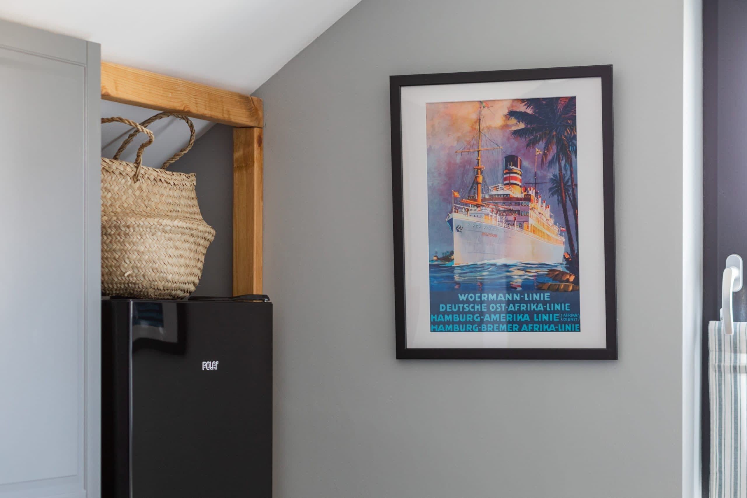 Un poster maritime encadré accroché au mur, un réfrigérateur noir et un panier en osier posé sur le dessus.