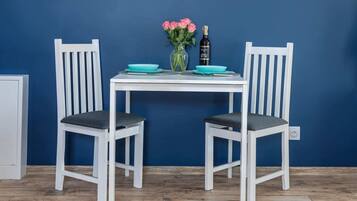 A dining table with two chairs, a vase with pink flowers, and a bottle of wine.