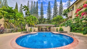A circular pool with a brick edge, surrounded by palm trees and a covered seating area.