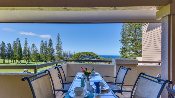 A balcony with a table set for two, overlooking a golf course and the ocean.