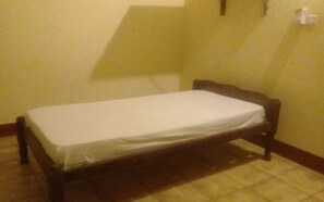 A small, single-bed room with a wooden bed frame and a white mattress. The room has a tiled floor and a plain yellow wall. - Kangs Hotel Malindi (Malindi)