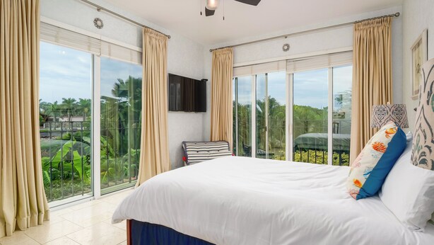 Un'ampia camera da letto con un letto grande, porte scorrevoli in vetro che si aprono su un balcone, una ventola a soffitto e una televisione a schermo piatto.