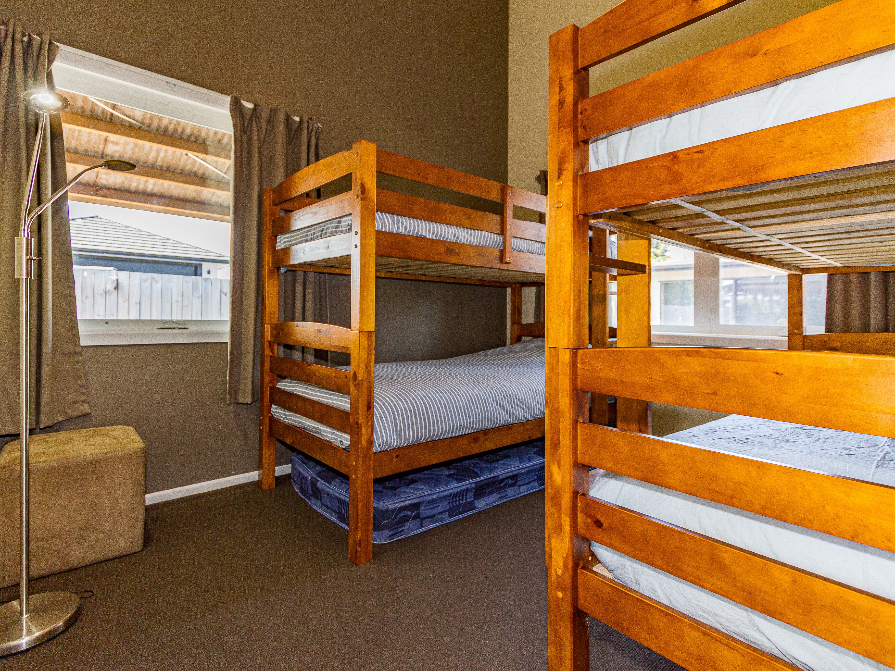 Una habitación con literas, una mesita de noche, una lámpara de pie y una ventana con cortinas.