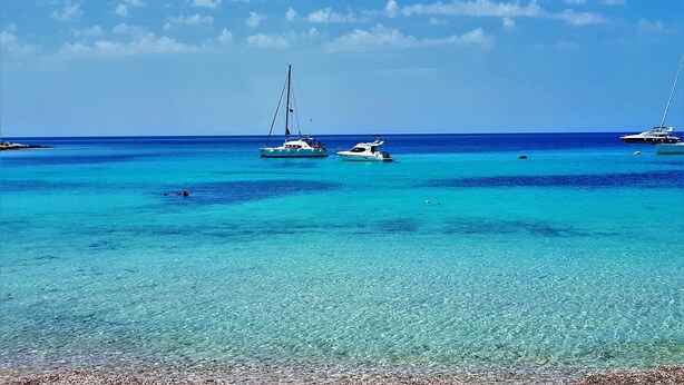 Une mer turquoise aux eaux limpides, parsemée de bateaux, et une plage de sable fin.