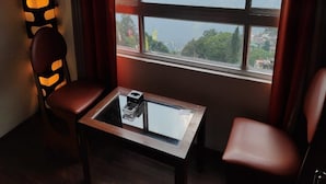 A room with a view of a mountainous landscape through large windows, a glass-top table with a small object on it, and two leather chairs.