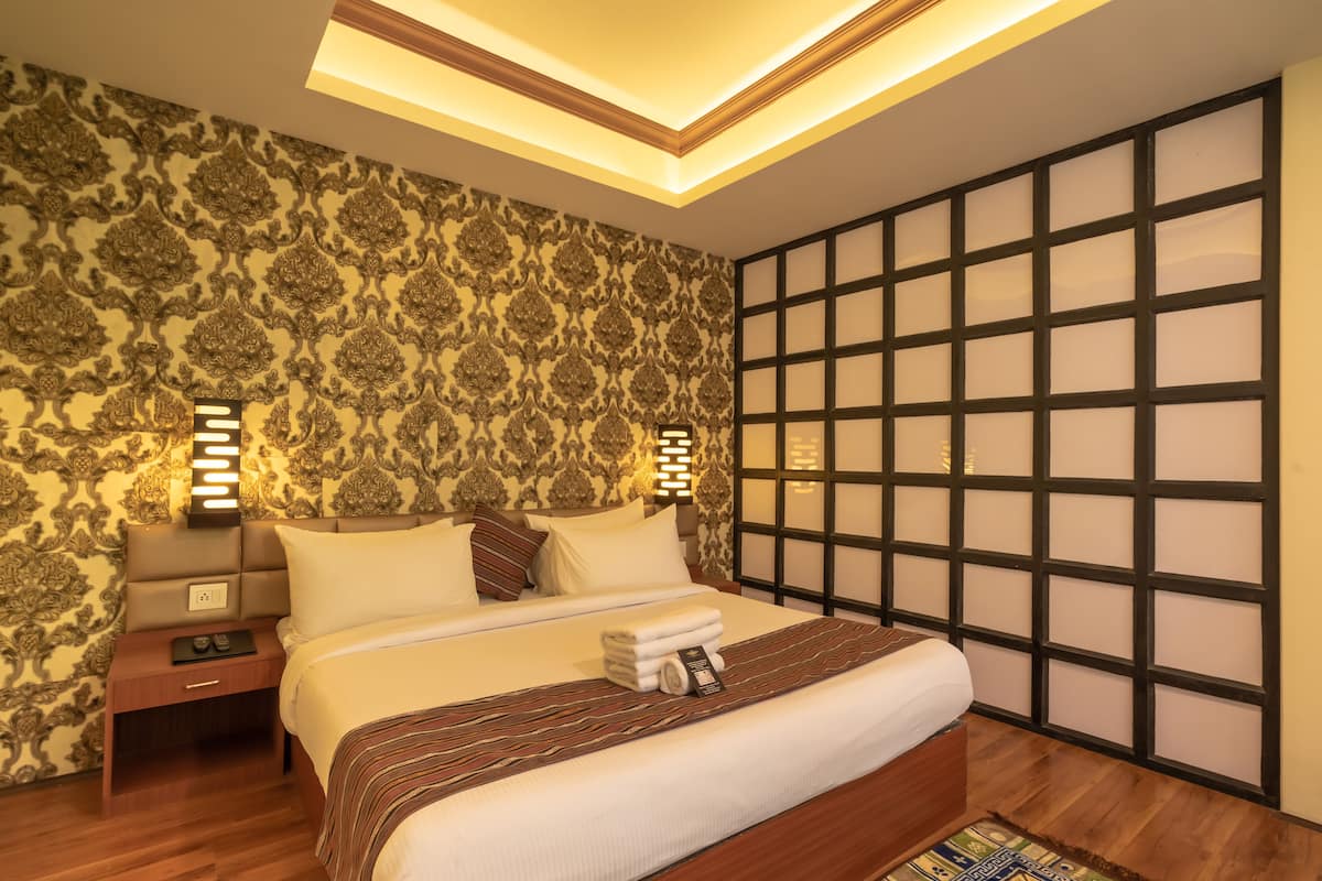 Un dormitorio moderno con una cama grande, papel tapiz estampado, cabecera de madera y una mesita de noche con lámpara.