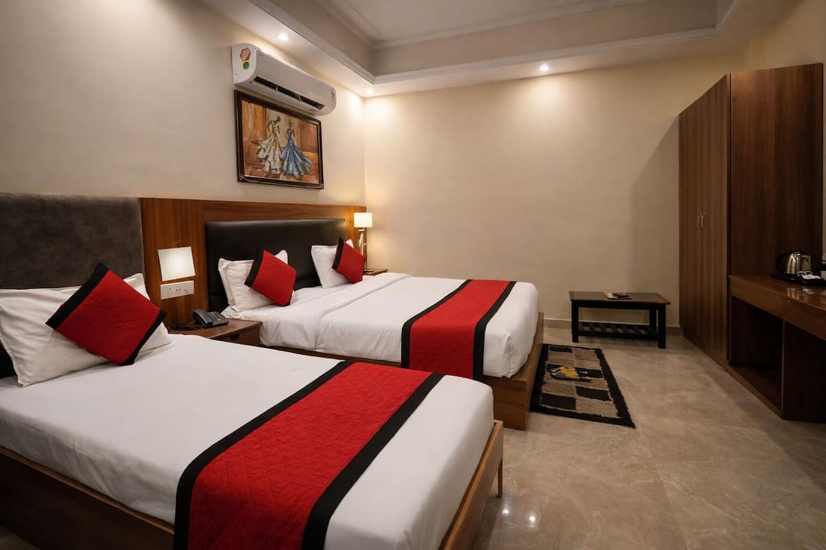A hotel room with two beds, a wooden wardrobe, a small table, and a painting on the wall.