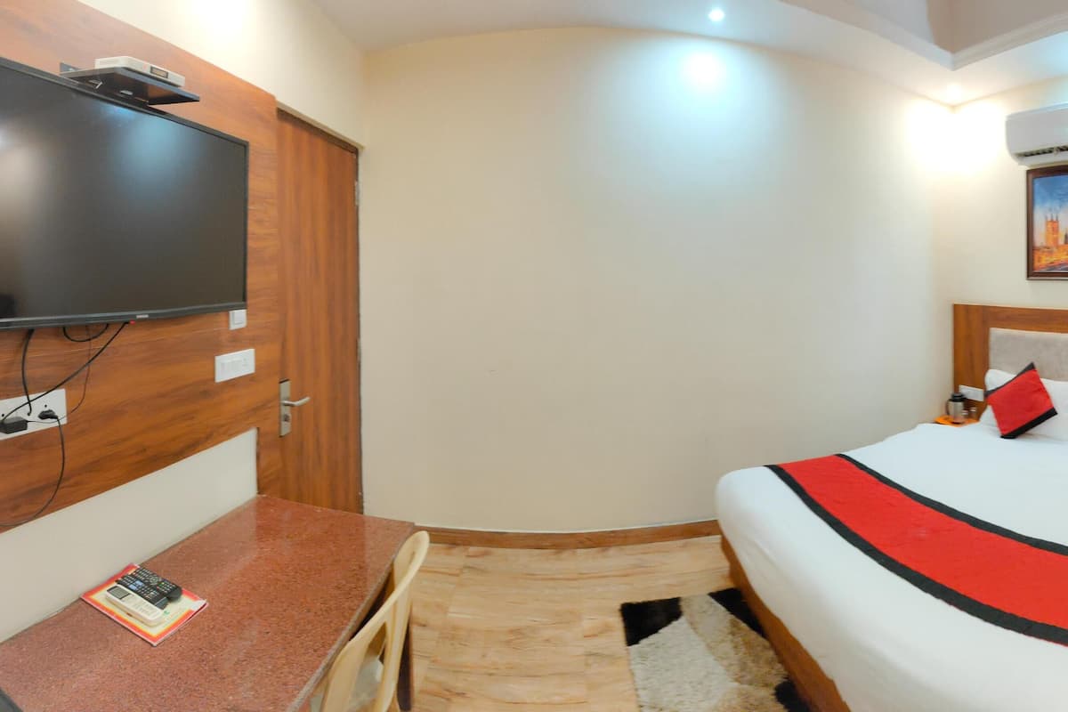 A hotel room with a bed, a desk, a television, and an air conditioning unit.