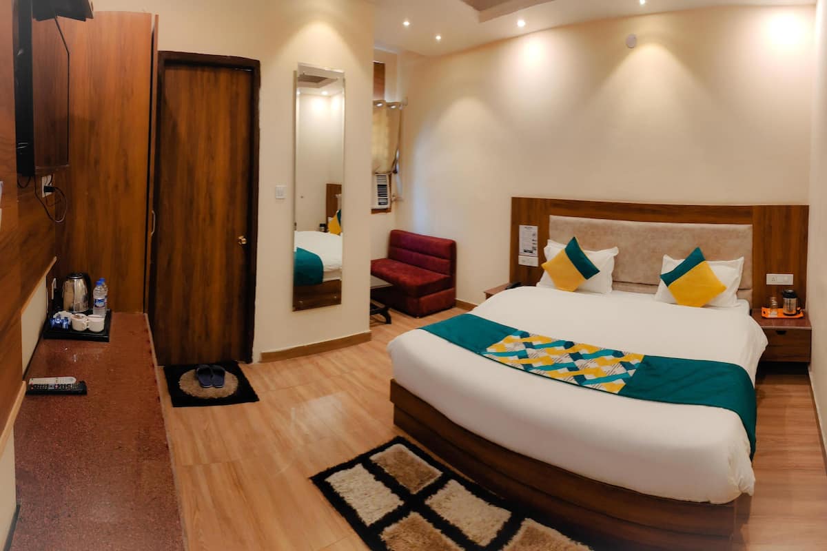A hotel room with a large bed, a wooden wardrobe, a red armchair, and a small table with a kettle and cups.