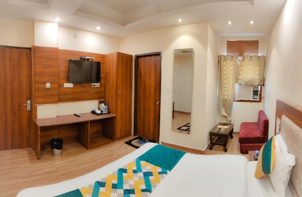 Quarto de hotel com uma cama, uma mesa, uma televisão, uma cadeira vermelha e uma janela com cortinas.