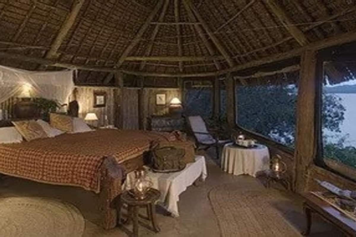 A cozy, thatched-roof bedroom with a bed, bedside tables, and a view of the outdoors.