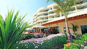 Un hotel con fachada curva, zona de estar al aire libre y jardín ajardinado con diversas plantas y flores.