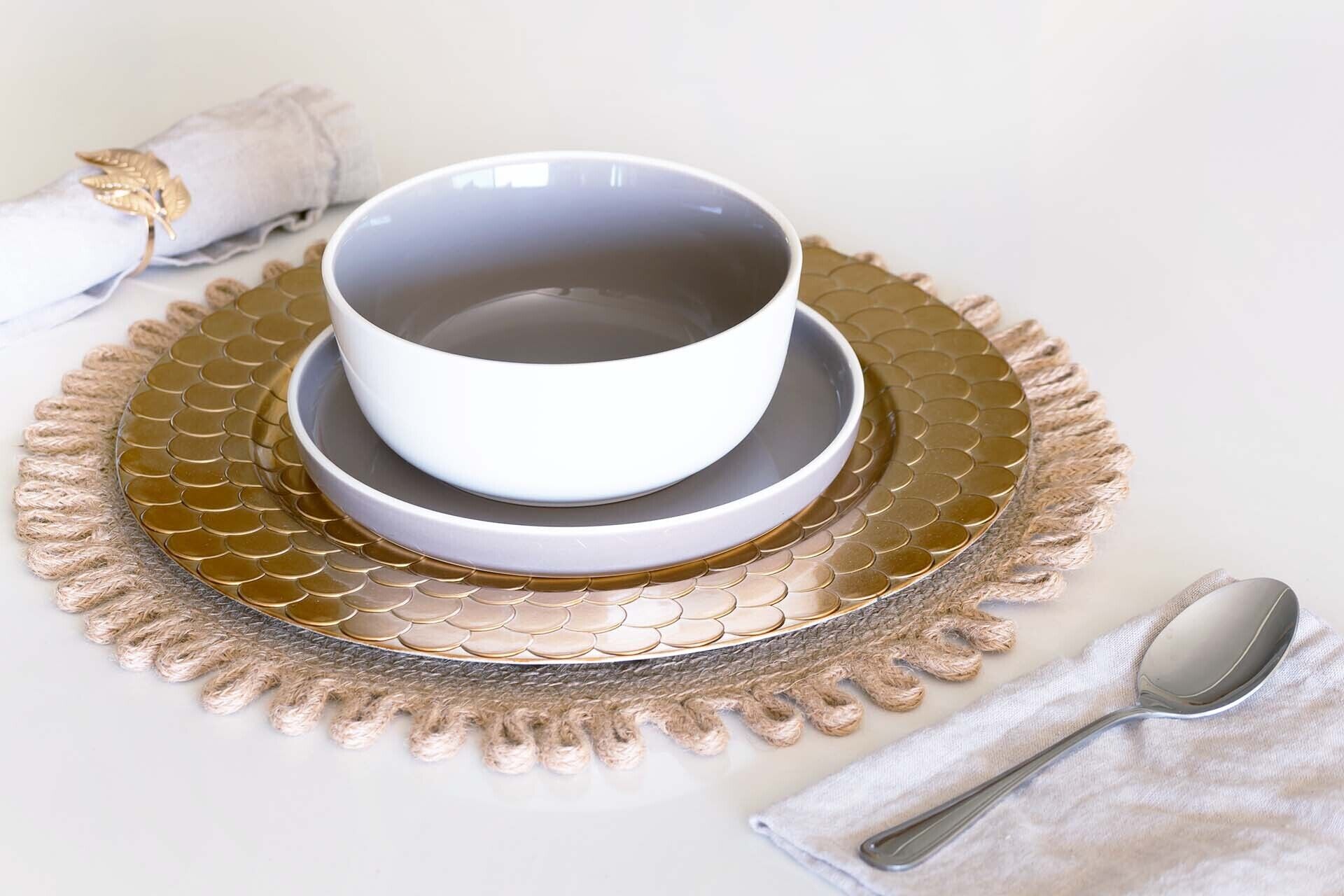 A white bowl on a gold plate with a scalloped edge, placed on a textured mat.
