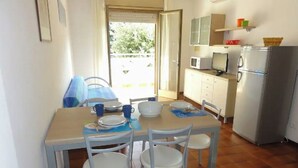 Un coin repas avec une table dressée pour quatre personnes, des chaises blanches, un four à micro-ondes, un réfrigérateur et une fenêtre donnant sur un paysage verdoyant.