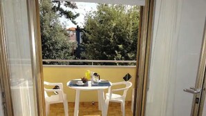 Un balcon ouvert avec une table et des chaises, donnant sur des arbres et un bâtiment en arrière-plan.