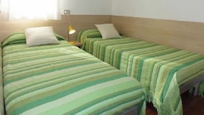Une chambre avec deux lits simples, chacun recouvert d’une couvre-lit à rayures vertes et agrémenté d’oreillers blancs. Une table de chevet avec une lampe jaune se trouve entre les deux lits.