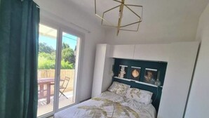 Et soveværelse med seng, loftlampe, skydedør og udsigt til en udendørs terrasse.
