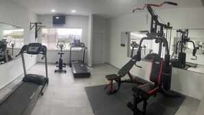 Ein Fitnessraum mit Laufbändern, Crosstrainern, einer Hantelbank und einem Spiegel.