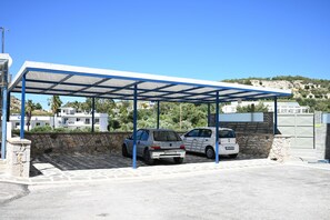 A covered parking area with two cars, stone walls, and a clear blue sky. - Ariadne Superior Suite | Views of Mount Filerimos ⛰️🦚🌿 (Kremasti, Rhodes)