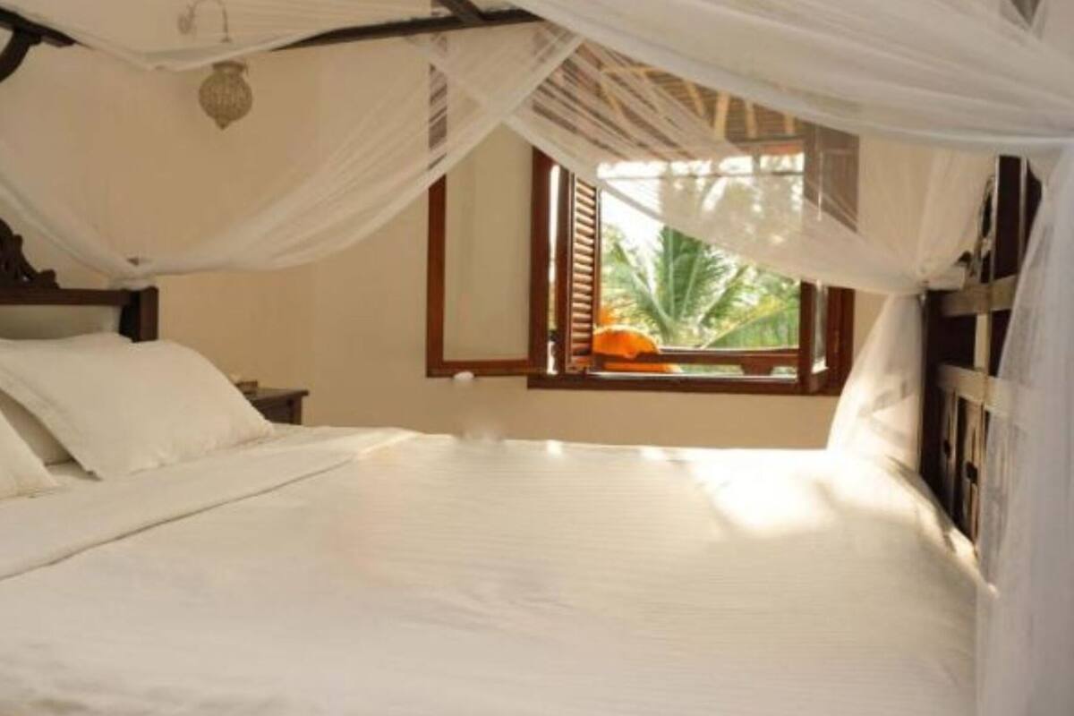 A bed with white linens and a canopy, a wooden headboard, and a window with a view of greenery.