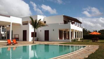 A modern two-story building with a swimming pool, outdoor seating, and a covered patio area.