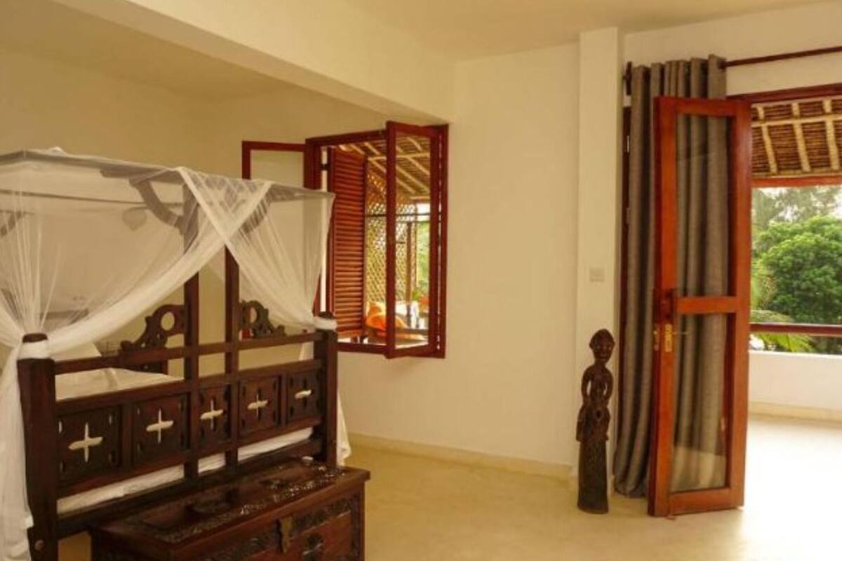 A room with a bed, a wooden nightstand, a small statue, and a window with wooden shutters.
