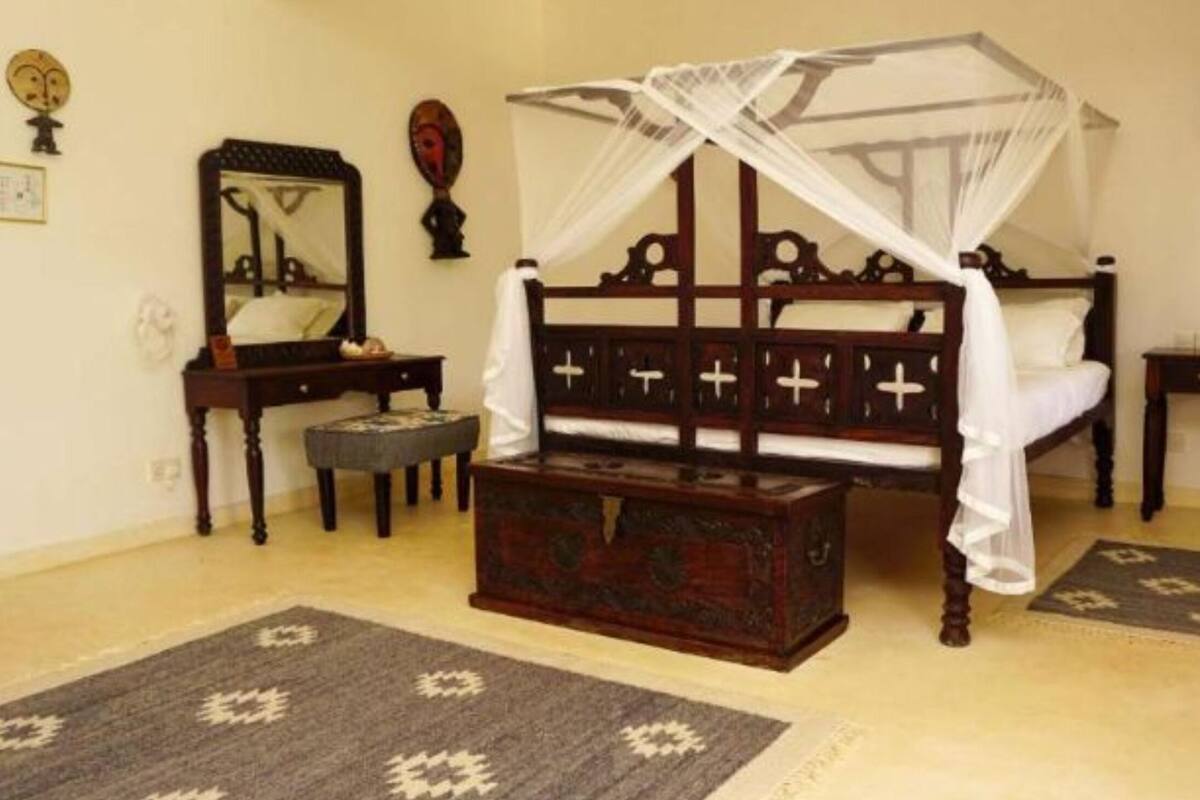 A traditional room with a four-poster bed, a wooden chest, a small table, and a mirror.