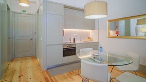 A modern kitchen with white cabinets, a built-in oven, and a glass dining table with white chairs. - Feel Porto Matosinhos Ocean Flat III (Matosinhos)