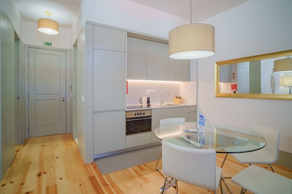 A modern kitchen with white cabinets, a built-in oven, and a glass dining table with white chairs.