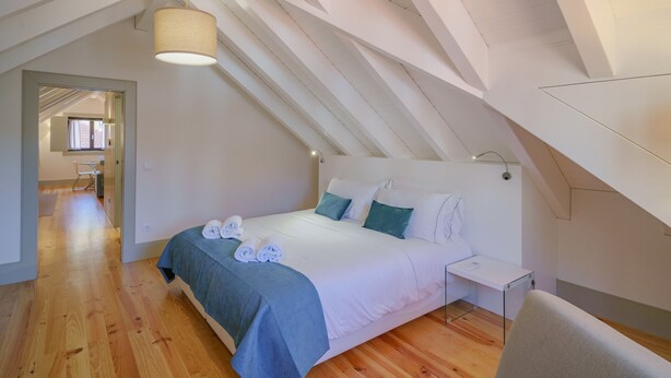 A bedroom with a sloped ceiling, a bed with blue bedding, a bedside table, and a hanging light fixture. - Feel Porto Matosinhos Ocean Flat IV (Matosinhos)