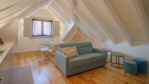 A modern loft bedroom with a sloped ceiling, a grey sofa, a small round table, and a window with curtains. - Feel Porto Matosinhos Ocean Flat IV (Matosinhos)