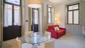 Una sala de estar moderna con una mesa de vidrio, sillas blancas, un sofá rojo y un ventanal con cortinas.