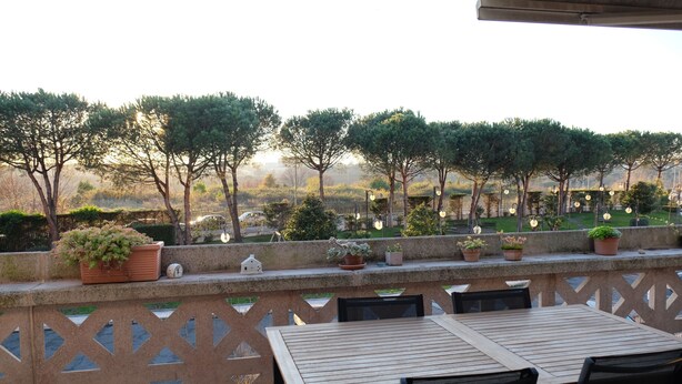 An outdoor patio with a wooden table and chairs, surrounded by potted plants and a decorative fence. - Green view penthouse with beautiful terrace and playground (Lazio)