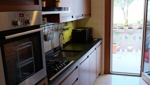 A modern kitchen with stainless steel appliances, wooden cabinets, and a large window providing natural light. - Green view penthouse with beautiful terrace and playground (Lazio)
