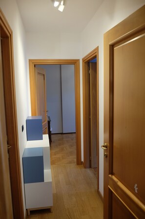 Een gang met houten deuren, een meubelstuk in wit en blauw, en een houten vloer.