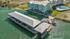 A waterfront hotel with a large building, a dock, and a pool area. - Jubilee Landing 303 | Boaters Welcome | Outdoor Pool | My Beach Getaways (Orange Beach)