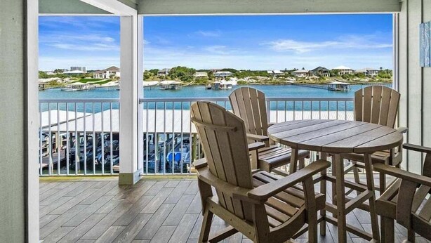 A covered outdoor area with a table and chairs, a ceiling fan, and a view of a marina with boats and houses. - Jubilee Landing 303 | Boaters Welcome | Outdoor Pool | My Beach Getaways (Orange Beach)