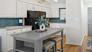 A modern kitchen with white cabinetry, a black refrigerator, a grey island with stools, and a decorative vase. - Jubilee Landing 303 | Boaters Welcome | Outdoor Pool | My Beach Getaways (Orange Beach)