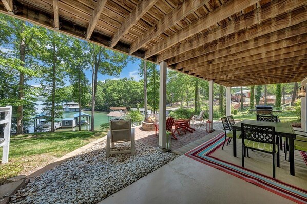 An outdoor patio with a view of a lake, surrounded by trees and a wooden deck.