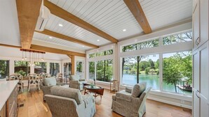 A spacious living room with wooden flooring, large windows, and a view of a lake. - Lake Grace - Lakefront, Private Dock & Hot Tub (Moneta)
