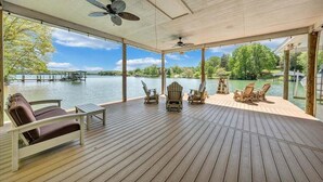 A covered deck with wooden flooring, ceiling fans, and Adirondack chairs overlooking a lake. - Lake Grace - Lakefront, Private Dock & Hot Tub (Moneta)